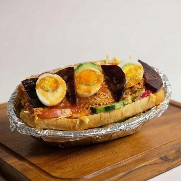 A Mexican torta with shredded meat, sliced eggs, and vegetables in a foil-lined tray on a wooden board.