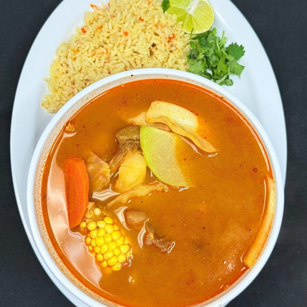 Hearty Mexican soup with corn, carrots, and meat, served with rice, cilantro, and lime.