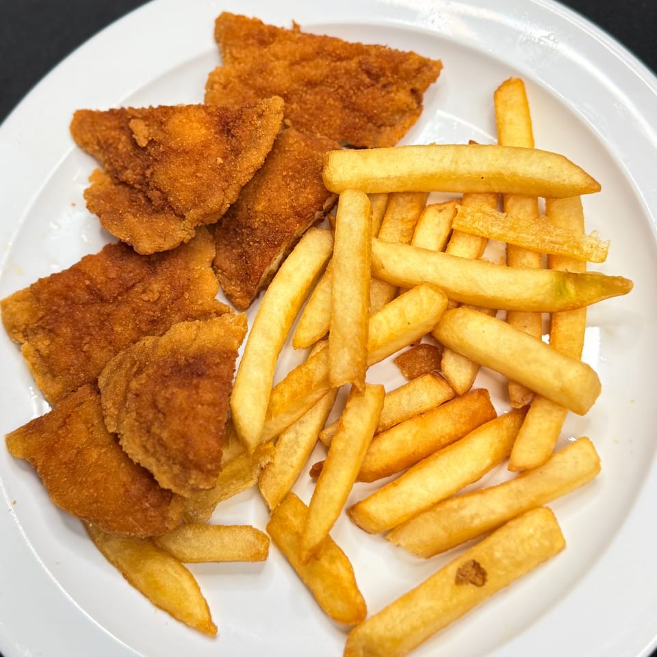 A white plate holds golden-brown breaded chicken cutlets and a pile of crispy french fries.