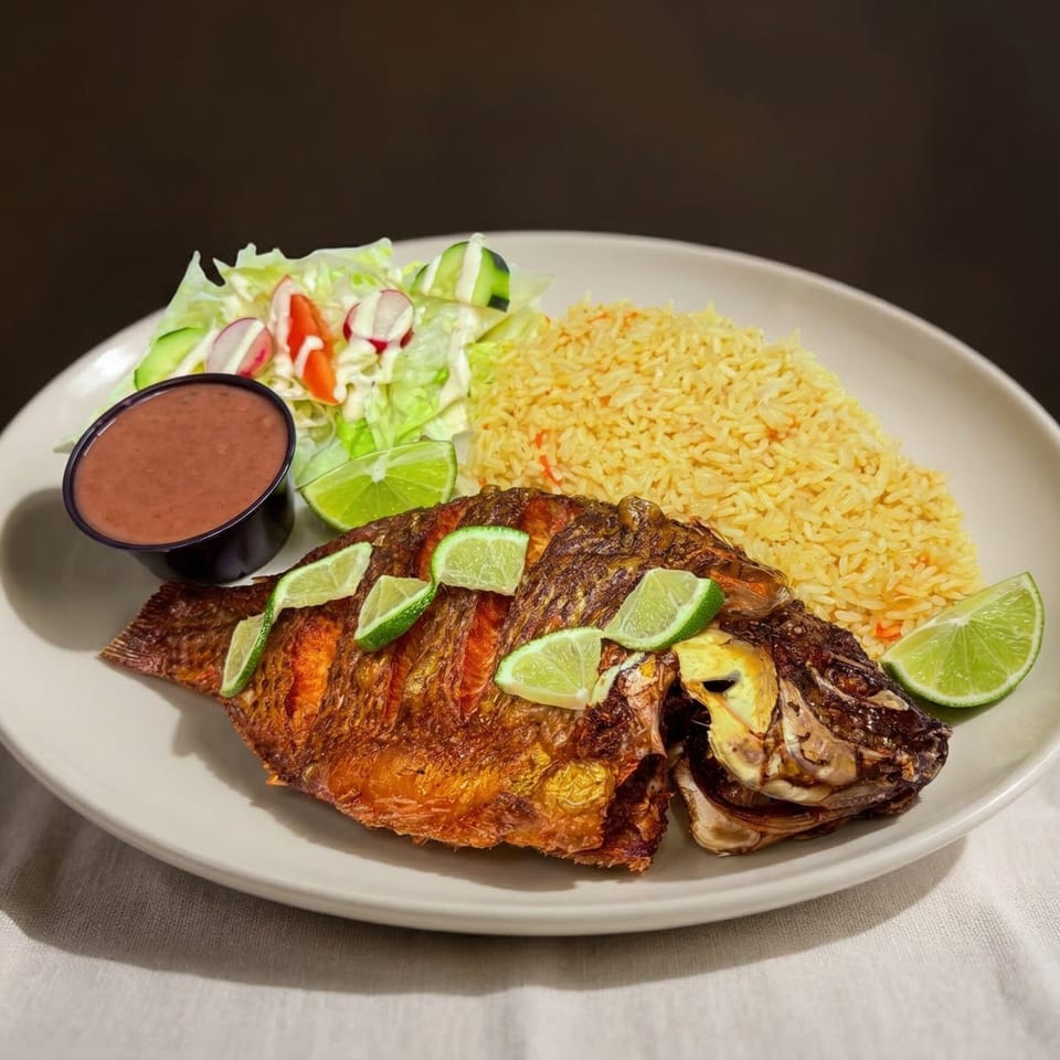 Whole fried tilapia with lime slices, yellow rice, a side salad, and red salsa.