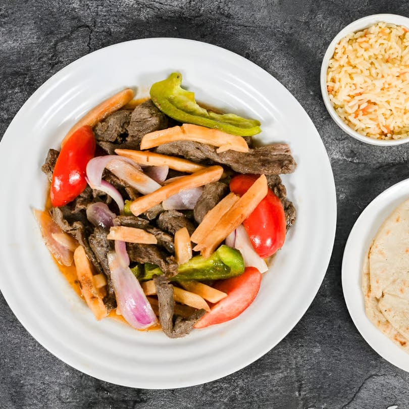 Mi Casita Restaurant's Lomo Saltado with steak, bell peppers, onions, fries, rice, and tortillas.