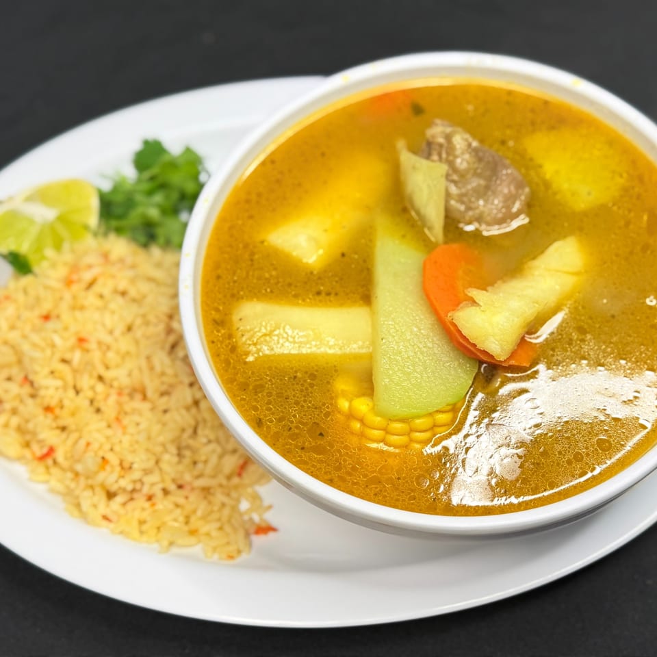 Hearty Mi Casita Mexican soup with beef, corn, chayote, carrots, and potatoes, served with rice and lime.