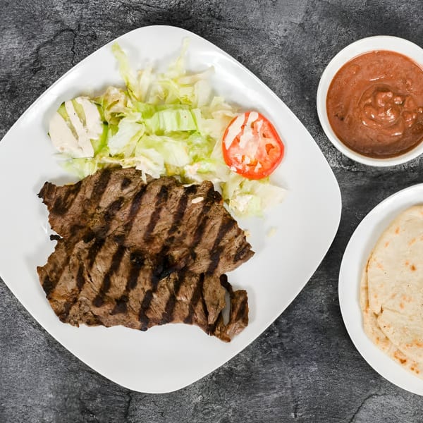 Grilled steak with lettuce, tomato, and cheese on a white plate, with salsa and tortillas.