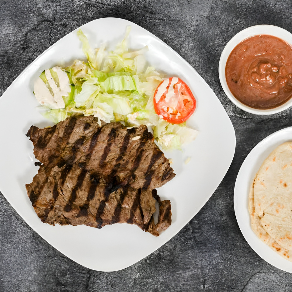 Grilled steak with lettuce, tomato, and cheese on a white plate, with salsa and tortillas.
